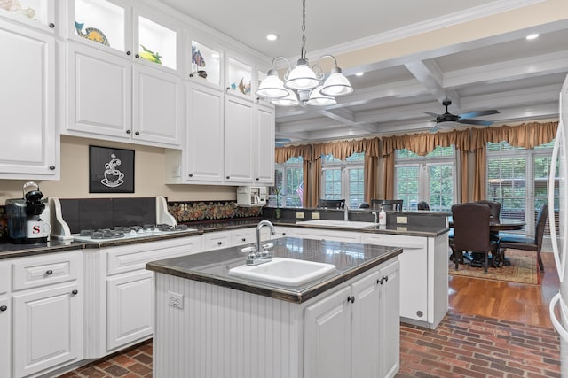 kitchen featuring a kitchen island with sink, ceiling fan with notable chandelier, decorative light fixtures, sink, and white cabinets