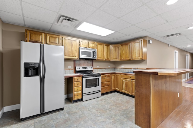 kitchen featuring appliances with stainless steel finishes, light hardwood / wood-style flooring, kitchen peninsula, and a drop ceiling