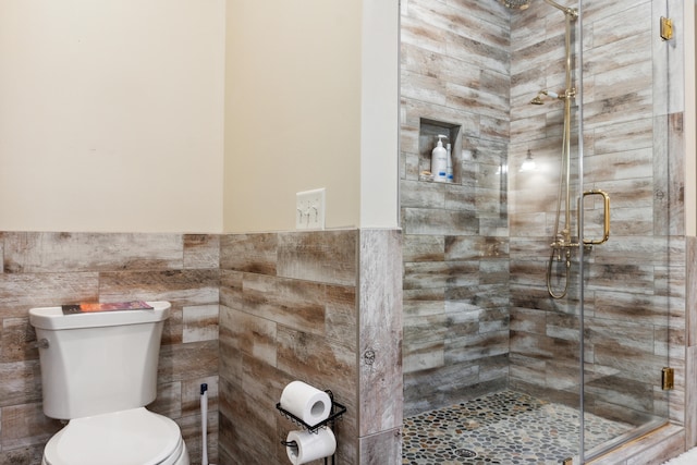 bathroom with tile walls, toilet, and a shower with shower door