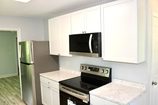 kitchen with light wood-type flooring, white cabinets, and appliances with stainless steel finishes