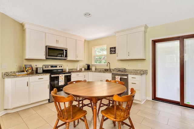 kitchen featuring stainless steel appliances, sink, light tile patterned floors, and white cabinetry