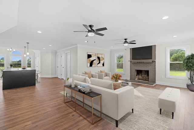 living room featuring hardwood / wood-style floors, ceiling fan with notable chandelier, a wealth of natural light, and a brick fireplace