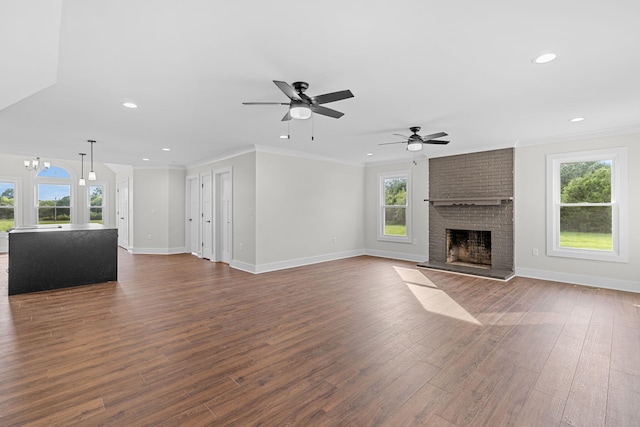 unfurnished living room featuring dark wood-type flooring, ceiling fan with notable chandelier, a fireplace, and a healthy amount of sunlight