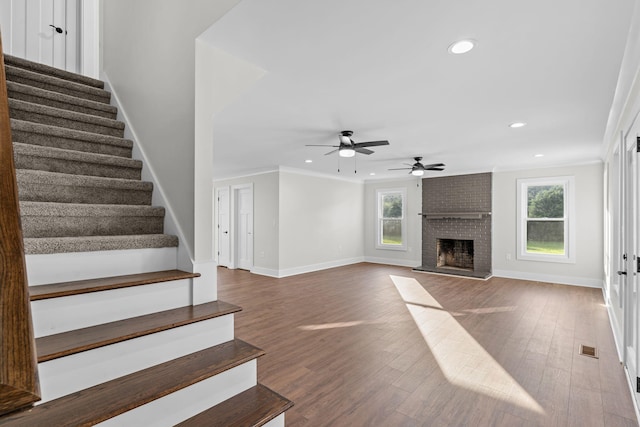 unfurnished living room with a fireplace, crown molding, wood-type flooring, and ceiling fan