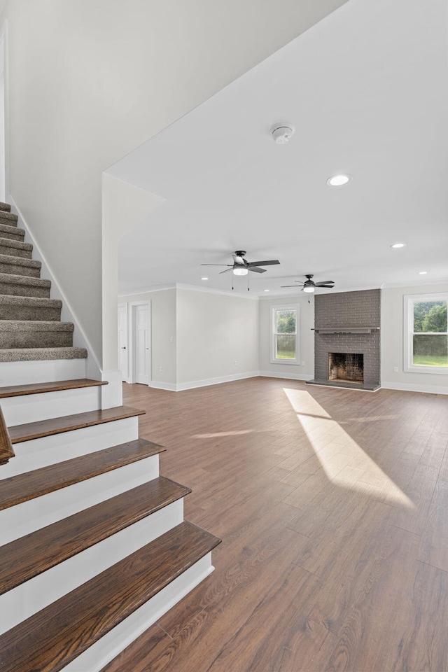 unfurnished living room with hardwood / wood-style flooring, a wealth of natural light, a brick fireplace, and ceiling fan