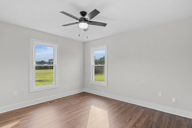 empty room with a healthy amount of sunlight, ceiling fan, and dark hardwood / wood-style floors