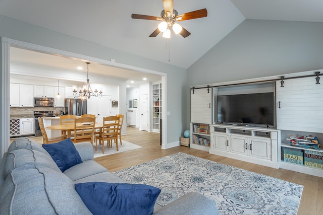 living room featuring a barn door, ceiling fan with notable chandelier, high vaulted ceiling, and light hardwood / wood-style floors