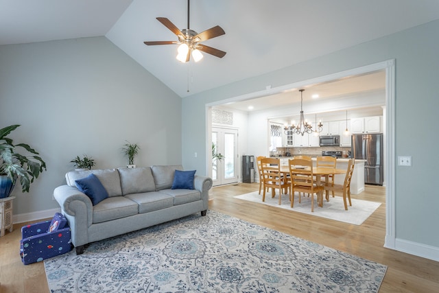 living room with high vaulted ceiling, ceiling fan with notable chandelier, and light hardwood / wood-style floors