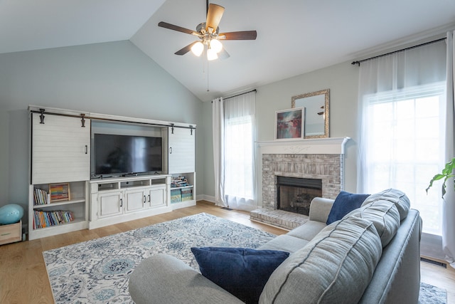 living room featuring lofted ceiling, ceiling fan, a brick fireplace, and light hardwood / wood-style flooring