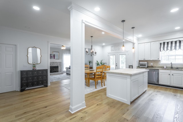 kitchen featuring a kitchen island, a stone fireplace, stainless steel dishwasher, white cabinetry, and light wood-type flooring