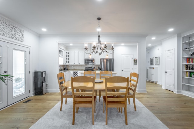 dining area with crown molding, an inviting chandelier, and light wood-type flooring