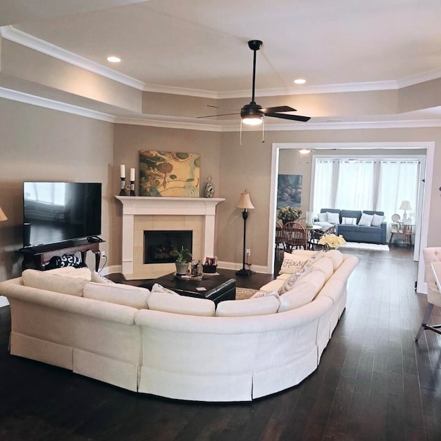 living room featuring a fireplace, ornamental molding, ceiling fan, dark hardwood / wood-style floors, and a tray ceiling