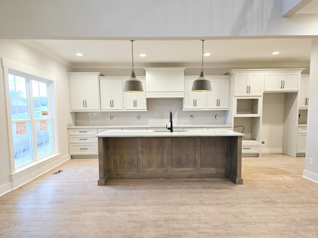 kitchen featuring sink, decorative light fixtures, white cabinetry, and an island with sink