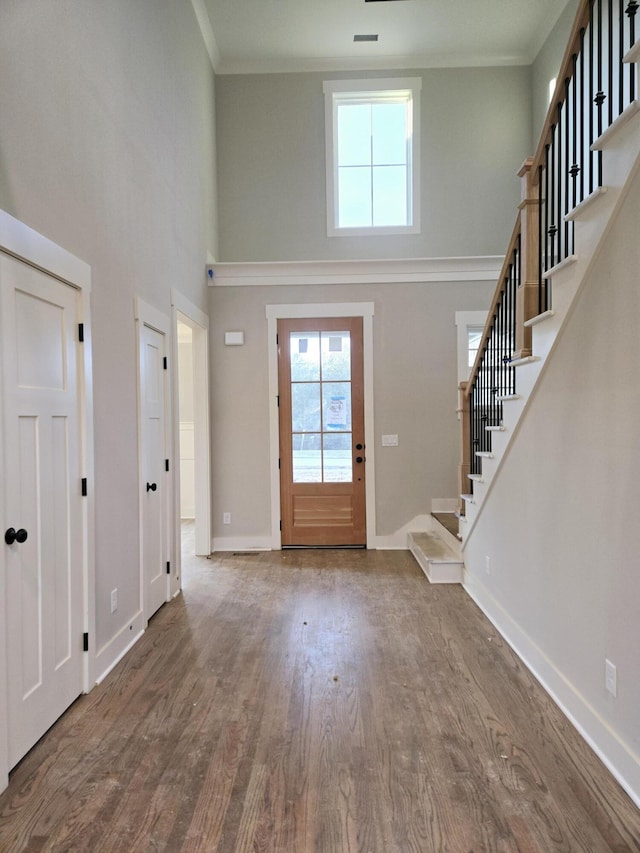 foyer entrance with hardwood / wood-style floors, a towering ceiling, and ornamental molding