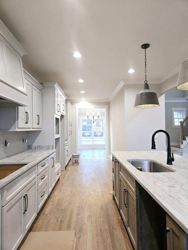 kitchen with light stone countertops, sink, plenty of natural light, light hardwood / wood-style floors, and decorative light fixtures