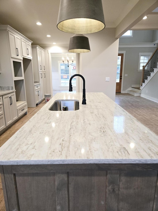 kitchen featuring wood-type flooring, light stone countertops, sink, and a large island with sink