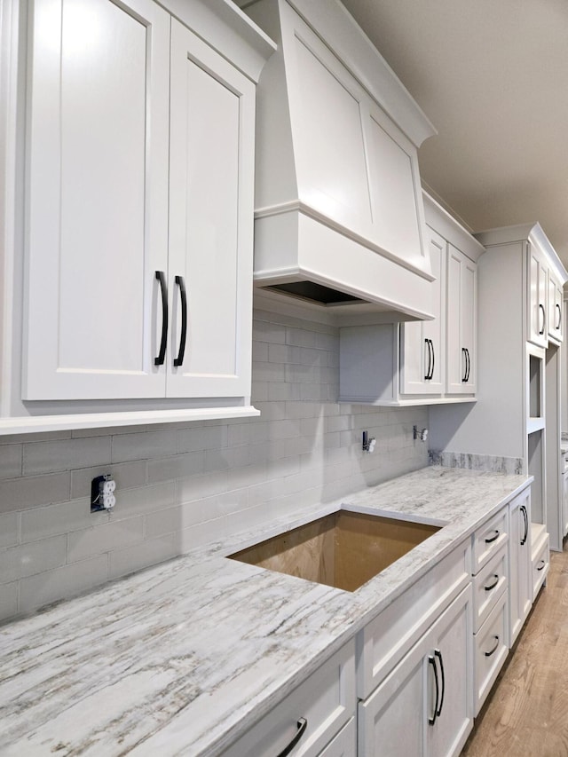 kitchen with white cabinets, light hardwood / wood-style floors, light stone counters, and custom range hood