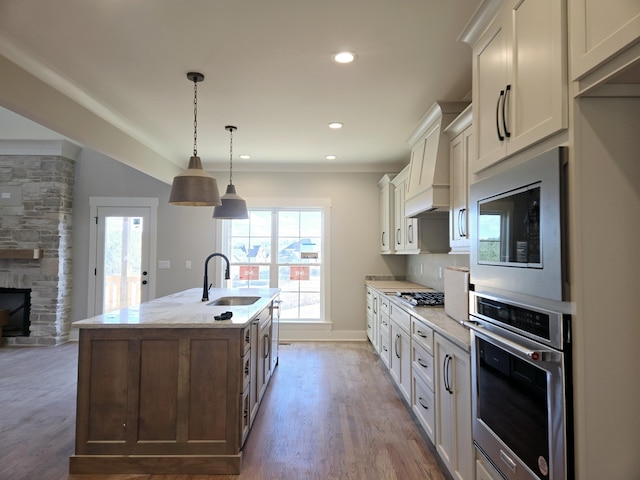 kitchen featuring appliances with stainless steel finishes, pendant lighting, sink, a kitchen island with sink, and light stone countertops