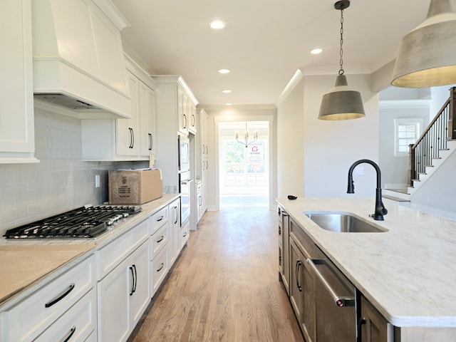 kitchen with sink, decorative light fixtures, custom range hood, stainless steel appliances, and white cabinets