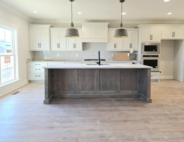 kitchen with stainless steel appliances, white cabinetry, a kitchen island with sink, and decorative light fixtures