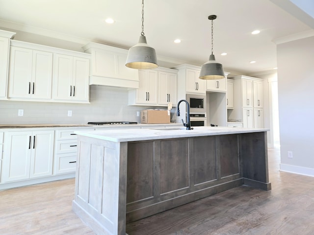 kitchen with sink, light hardwood / wood-style floors, white cabinets, a center island with sink, and decorative light fixtures