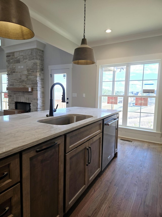 kitchen with sink, light stone counters, dishwasher, pendant lighting, and a fireplace