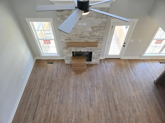 unfurnished living room with a stone fireplace, hardwood / wood-style floors, and ceiling fan