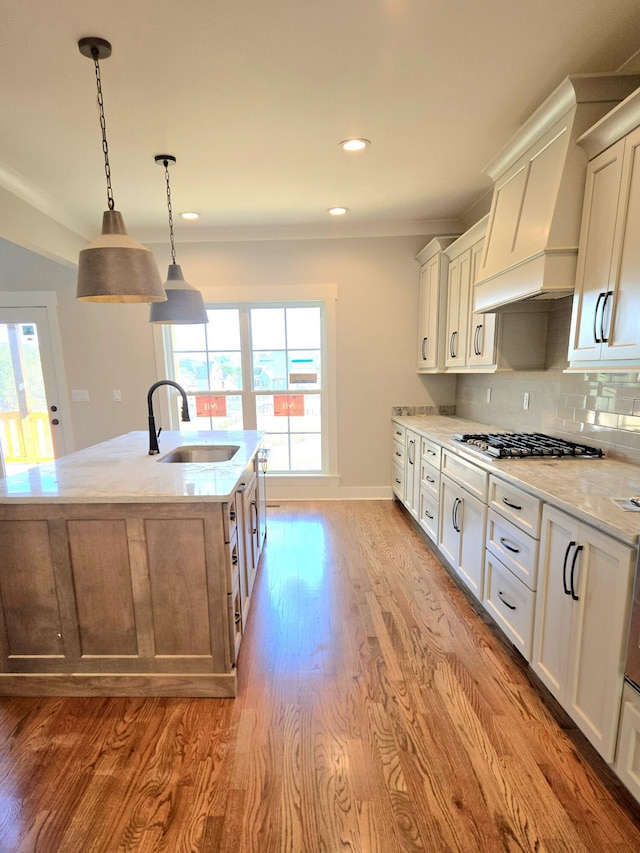 kitchen featuring stainless steel gas cooktop, custom exhaust hood, light stone counters, decorative backsplash, and a sink