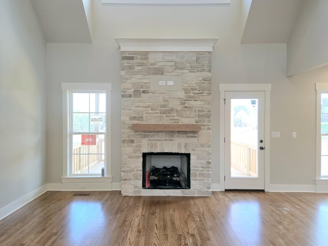 unfurnished living room featuring a towering ceiling, wood finished floors, a stone fireplace, and baseboards