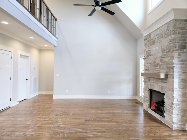 unfurnished living room featuring a towering ceiling, ceiling fan, a wealth of natural light, and a stone fireplace