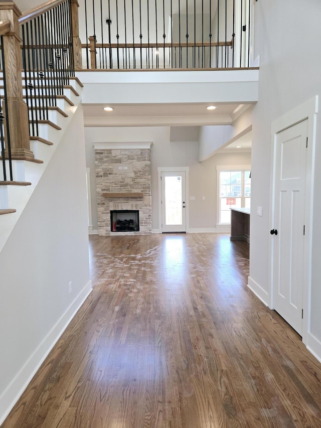 unfurnished living room featuring a high ceiling, stairway, a fireplace, baseboards, and wood finished floors