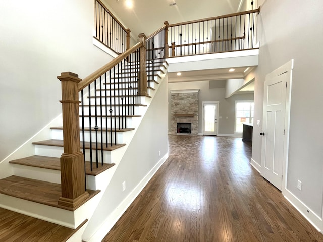 stairs featuring a fireplace, a towering ceiling, wood finished floors, and baseboards