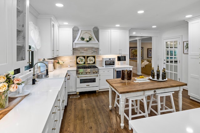 kitchen featuring designer stove, premium range hood, white cabinets, and dark wood-type flooring