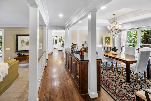 hall featuring hardwood / wood-style floors, ornamental molding, an inviting chandelier, a raised ceiling, and ornate columns