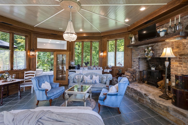 interior space featuring a wood stove, wood walls, a notable chandelier, and dark tile patterned flooring