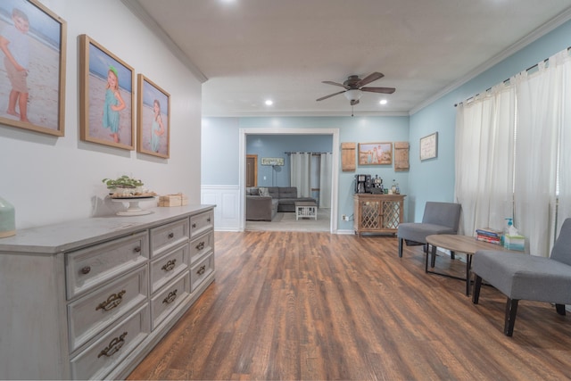 living area with a wainscoted wall, a ceiling fan, dark wood finished floors, and crown molding