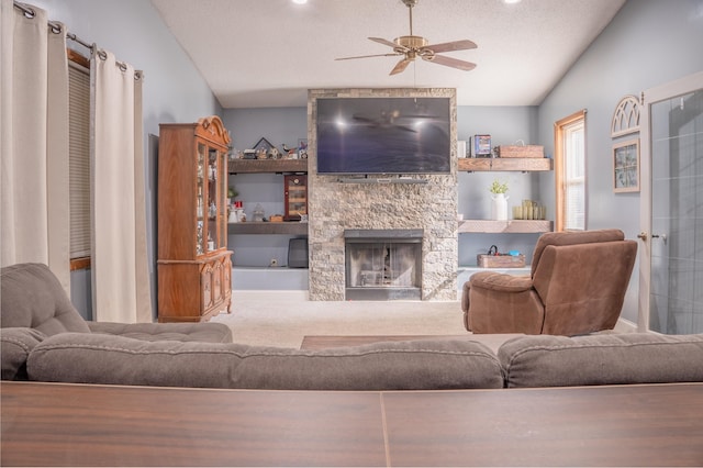 living area with lofted ceiling, ceiling fan, a stone fireplace, and a textured ceiling