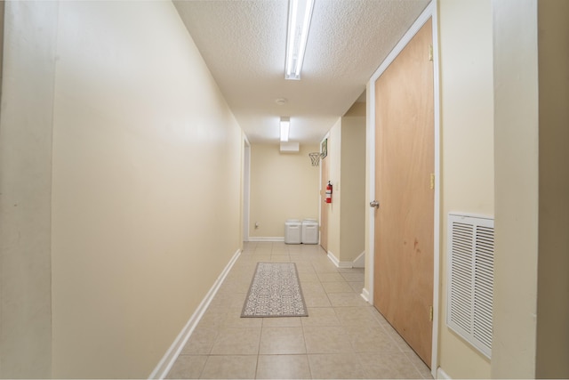 hall featuring visible vents, a textured ceiling, baseboards, and light tile patterned flooring