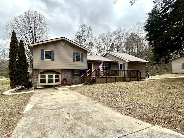 tri-level home with stairs, driveway, brick siding, and a wooden deck