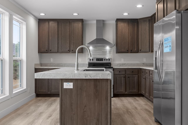 kitchen with appliances with stainless steel finishes, light wood-type flooring, wall chimney exhaust hood, and a center island with sink