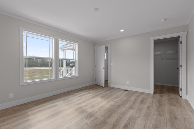 unfurnished bedroom with light hardwood / wood-style flooring, crown molding, a closet, and a spacious closet