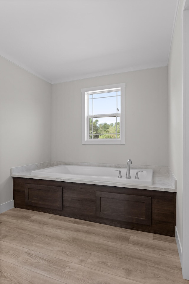 bathroom featuring wood-type flooring, crown molding, and a tub to relax in