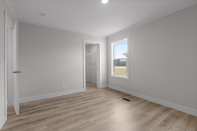 unfurnished bedroom with light wood-type flooring, crown molding, a closet, and a walk in closet