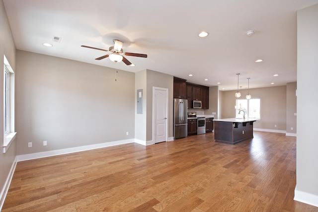 kitchen featuring light wood-type flooring, appliances with stainless steel finishes, ceiling fan, a center island with sink, and dark brown cabinetry