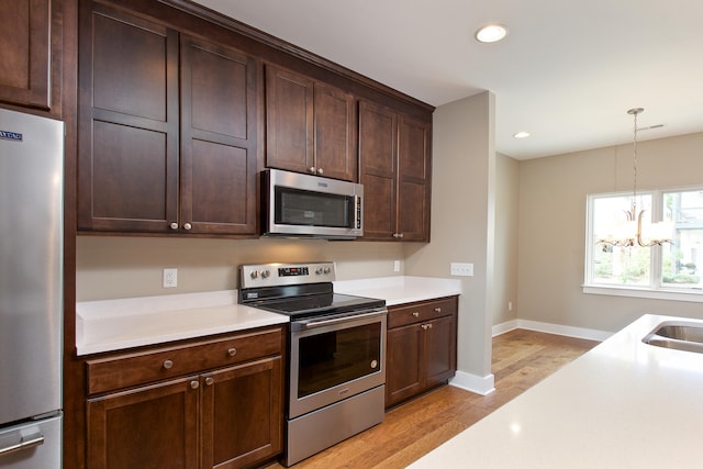 kitchen featuring stainless steel appliances, light hardwood / wood-style floors, a chandelier, sink, and pendant lighting