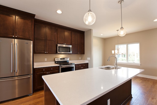 kitchen with sink, appliances with stainless steel finishes, hardwood / wood-style flooring, and a kitchen island with sink