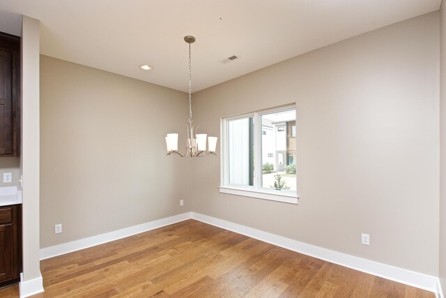 unfurnished dining area with hardwood / wood-style floors and a chandelier