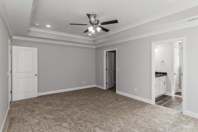 unfurnished bedroom with a raised ceiling, dark colored carpet, ensuite bathroom, and ceiling fan