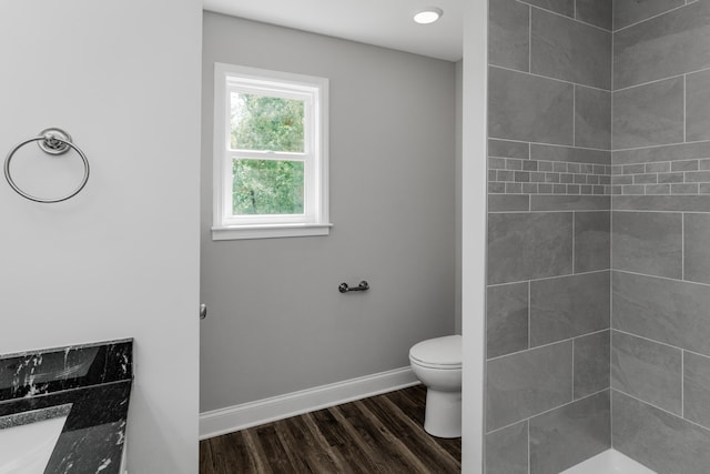 bathroom with wood-type flooring, vanity, a tile shower, and toilet