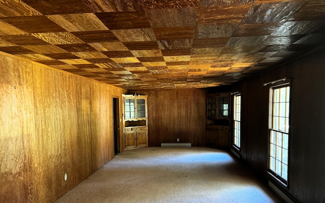 carpeted spare room featuring wooden walls and a baseboard radiator